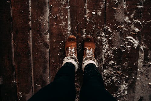 Person Wearing Brown Shoes and Black Pants Standing on Brown Wooden Planks