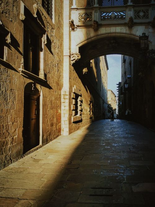 Free Ancient stone archway over a narrow alley in a sunlit historic European street. Stock Photo