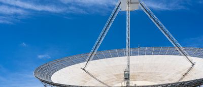 A large satellite dish points upward against a clear blue sky.