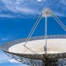 A large satellite dish points upward against a clear blue sky.