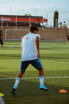 A young male athlete trains on a soccer field, focusing on footwork and agility drills.