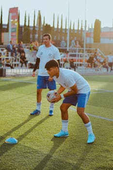 Two young men practicing soccer on an outdoor field during the day.