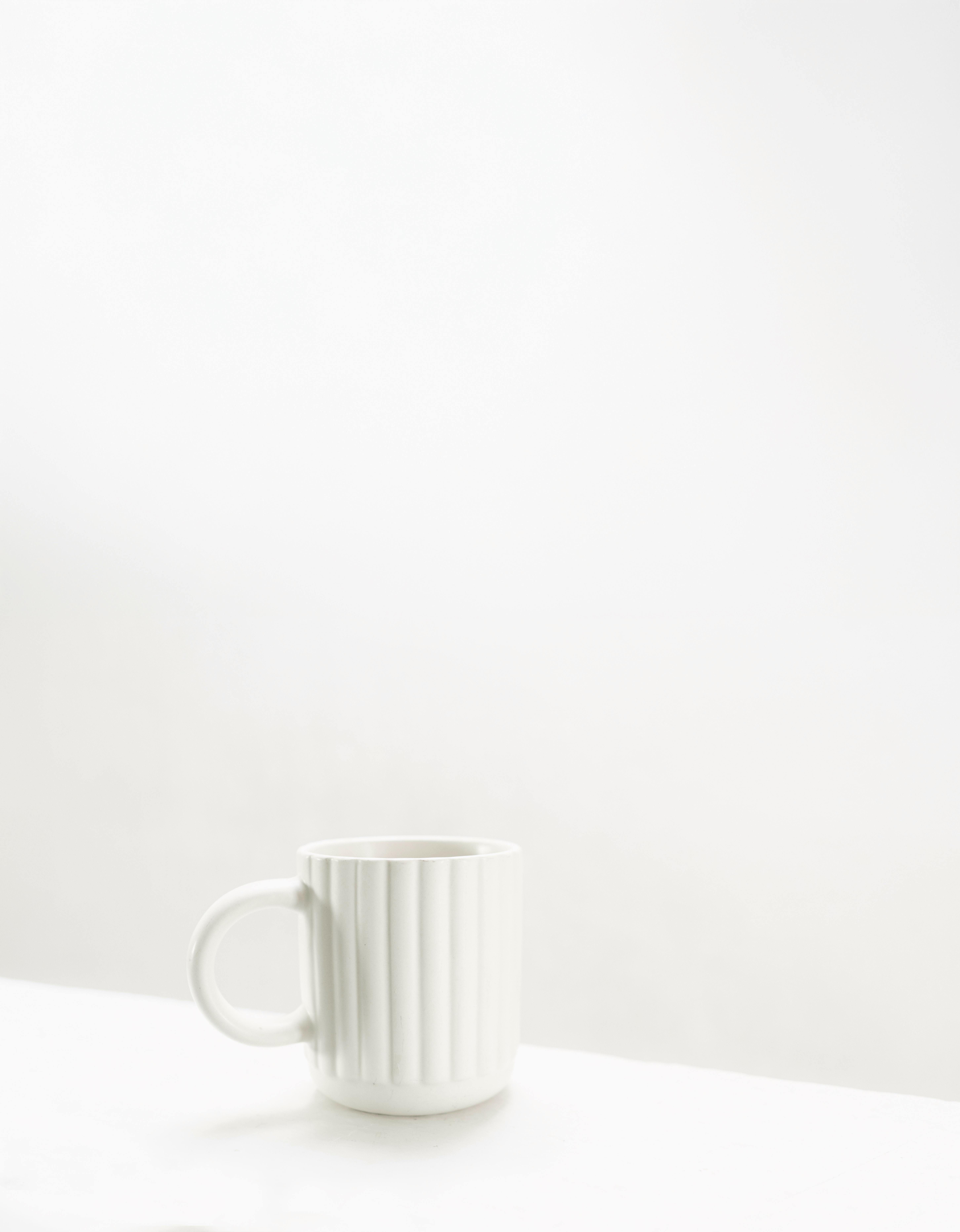 A simple, elegant white ceramic mug on a pristine white surface against a light background.