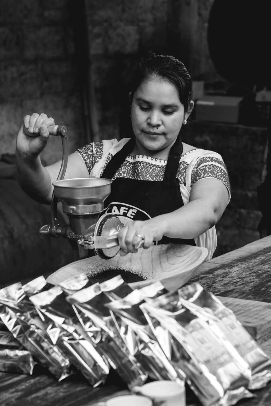 Woman processing coffee beans with manual grinder in cafe. Black and white.