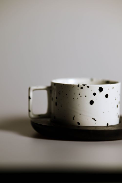 Free A stylish black and white speckled ceramic coffee cup on a matching saucer, perfect for minimalist decor. Stock Photo