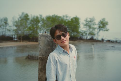 Free A young man wearing sunglasses poses by a river with lush green trees in Ho Chi Minh City. Stock Photo