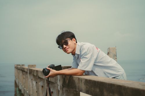 Free Young man with camera at a pier in Ho Chi Minh City, enjoying the view and capturing memories. Stock Photo