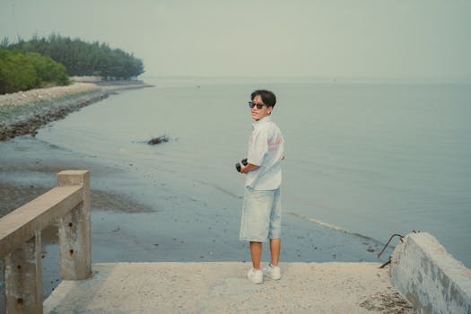 Young man in casual attire stands by the sea in Ho Chi Minh City, capturing a serene coastal scene.