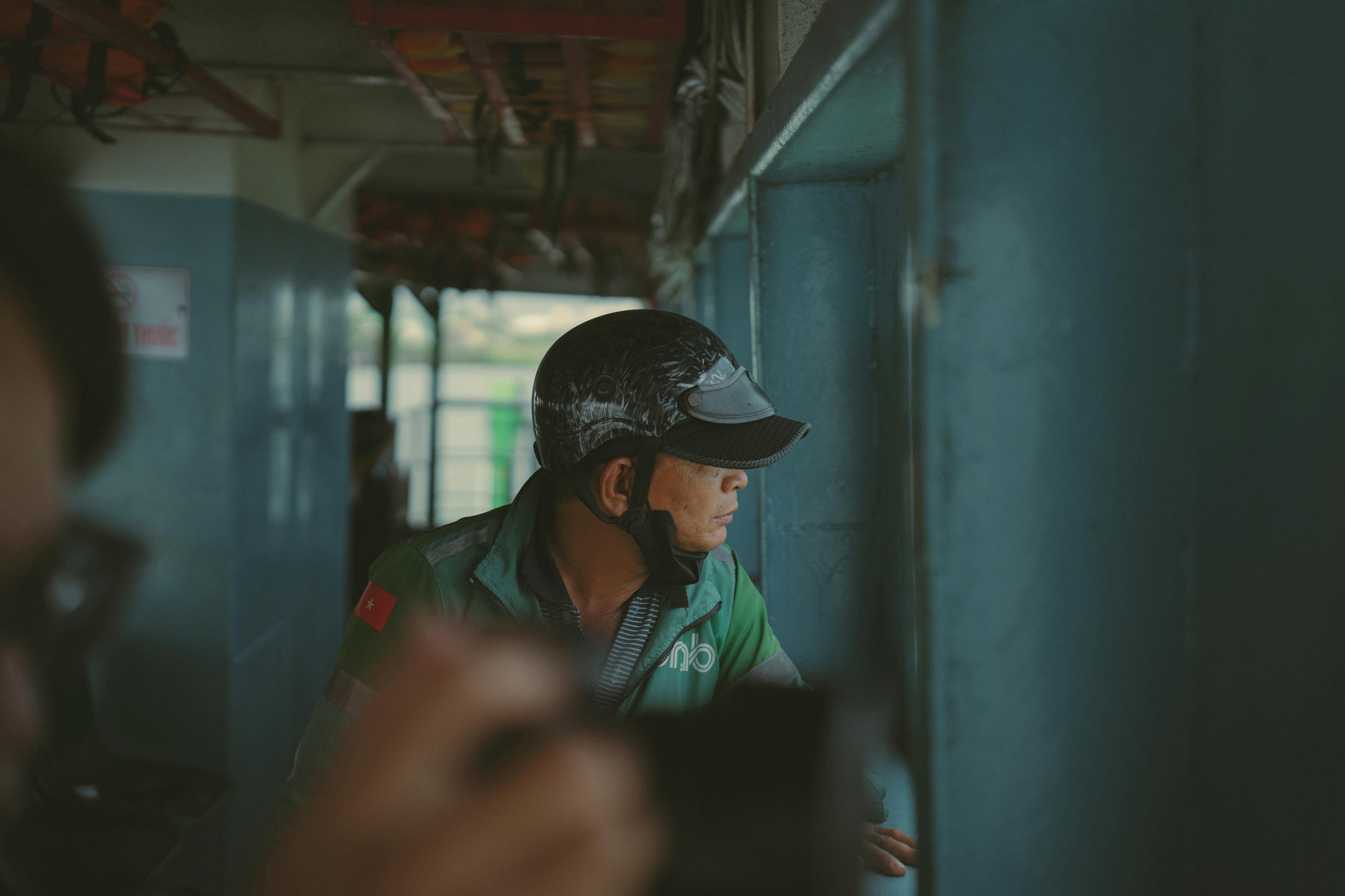 Kostnadsfria Man som bär en hjälm tittar ut genom ett fönster och fångar ett reflekterande ögonblick på en färja i Ho Chi Minh City, Vietnam. Stock foto