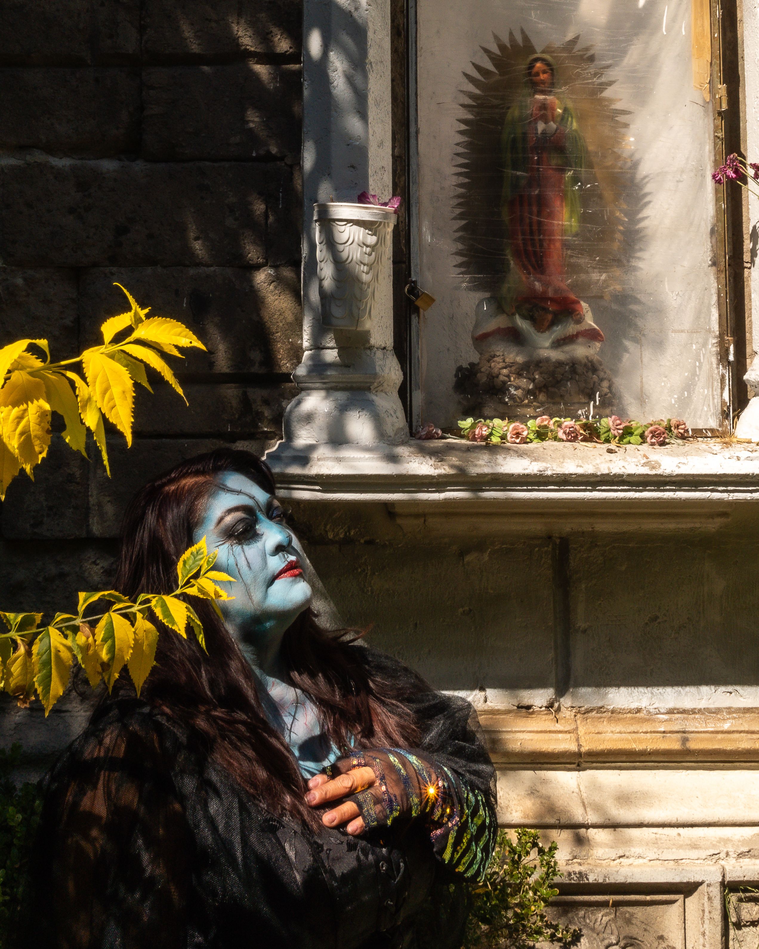 Surreal outdoor portrait with vibrant makeup near a religious icon in Mexico City.