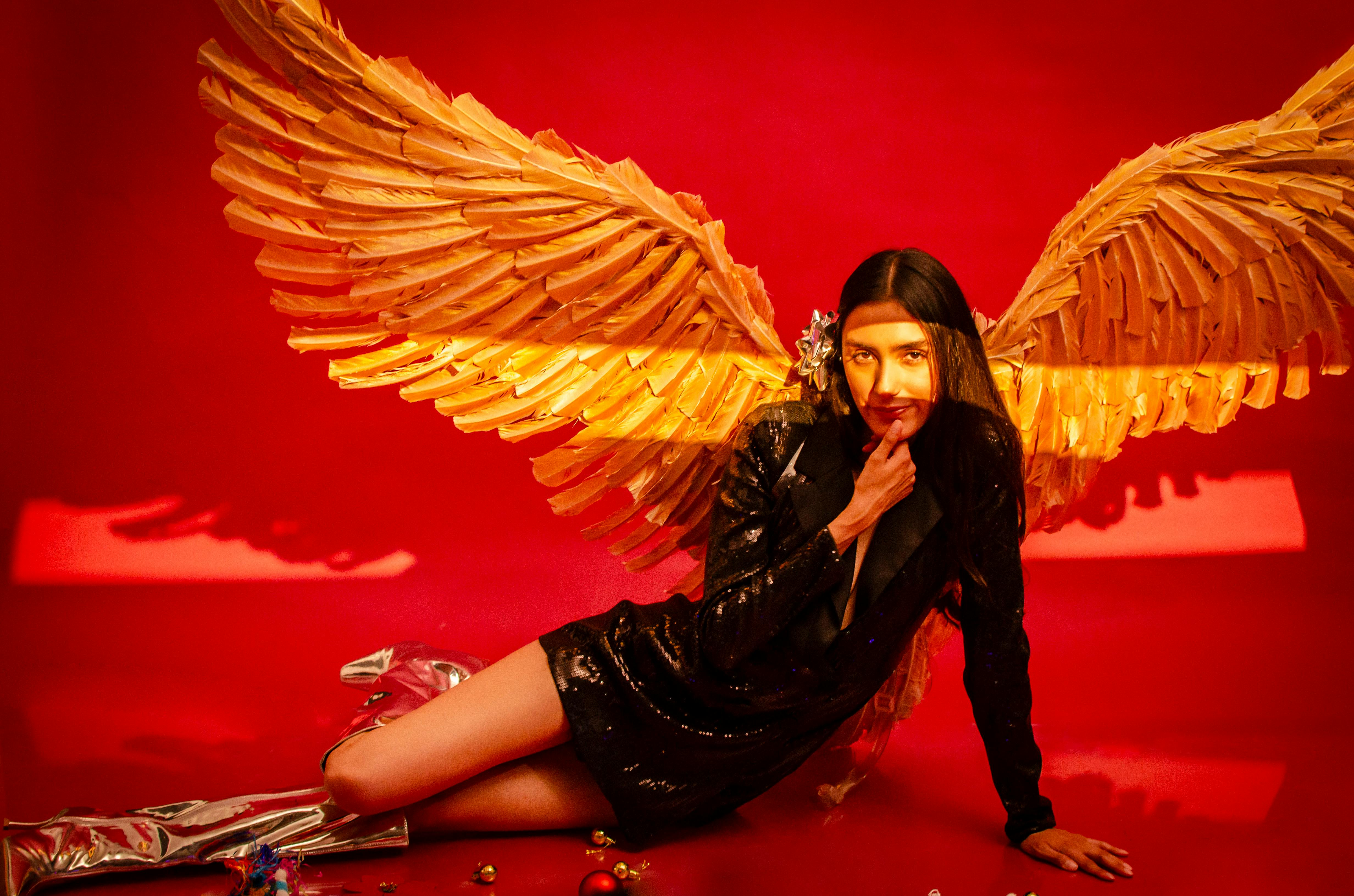 Bezpłatne Modna kobieta pozuje ze złotymi skrzydłami, tworząc oszałamiającą kompozycję artystyczną na jaskrawo czerwonym tle. Zdjęcie z galerii