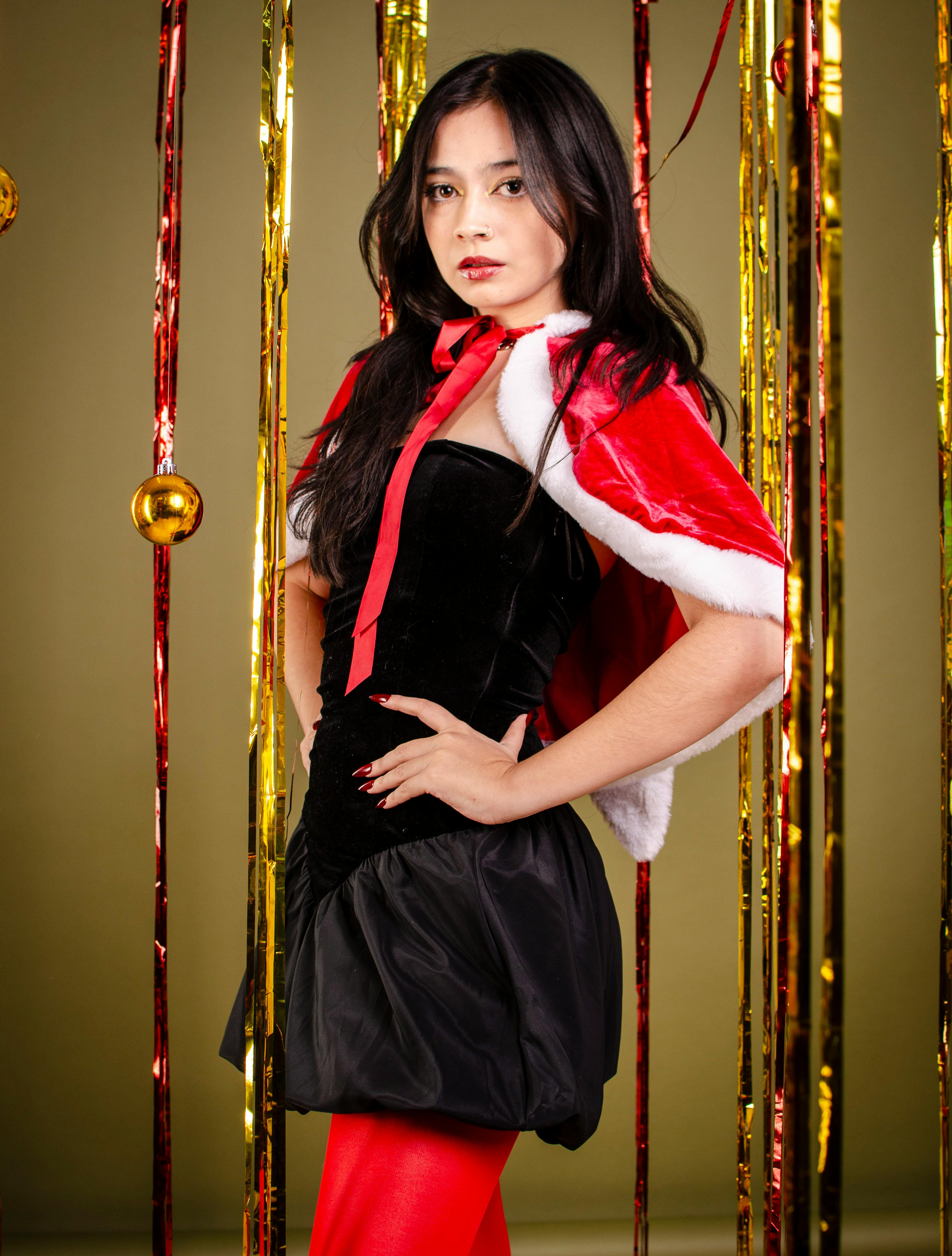 grátis Uma mulher estilosa usando uma roupa temática de Papai Noel posando com decorações natalinas em um ambiente interno. Foto profissional