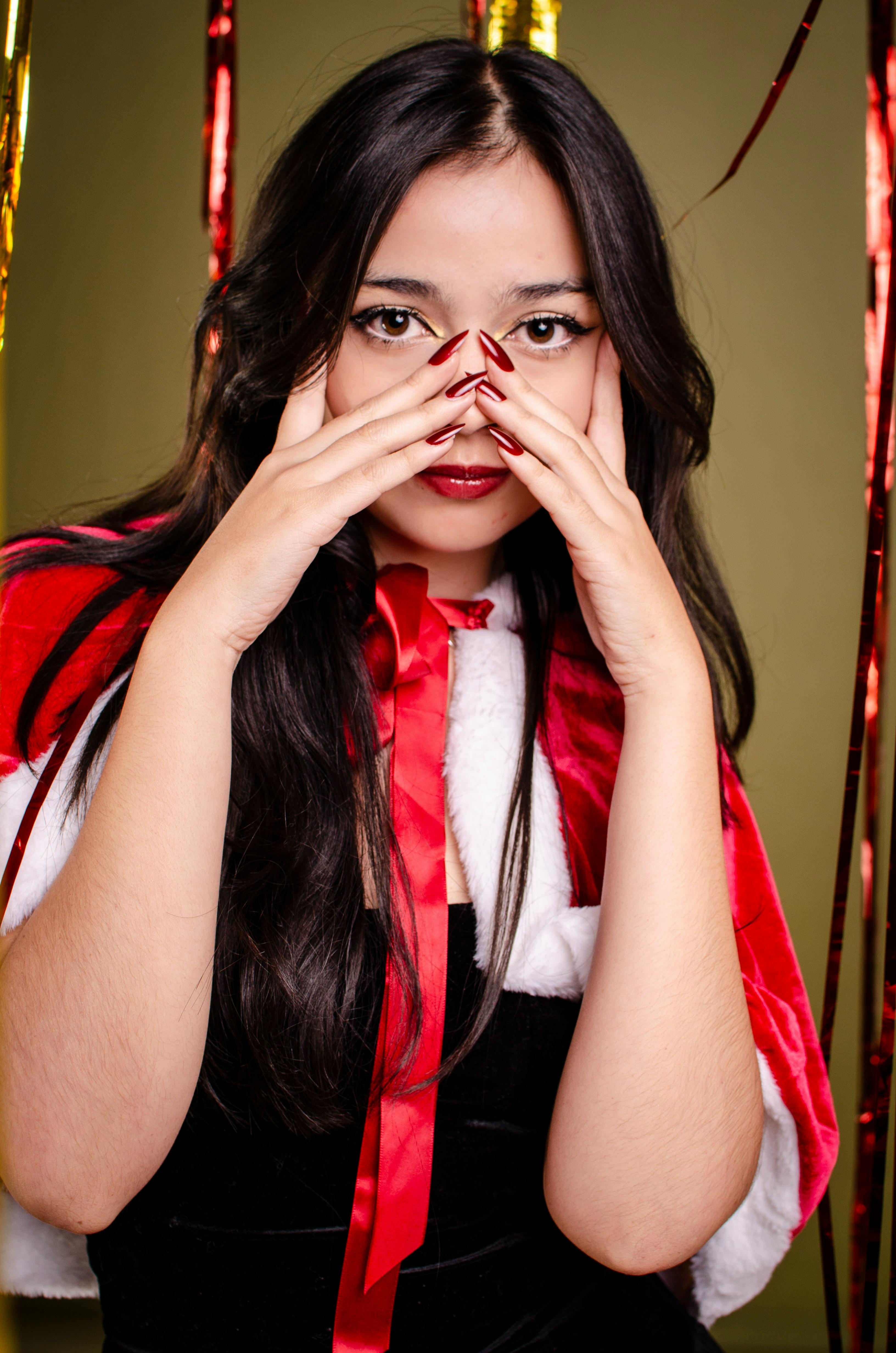 Bezpłatne Elegancki portret kobiety w pelerynie Świętego Mikołaja, świętującej Boże Narodzenie z czerwonymi paznokciami. Zdjęcie z galerii