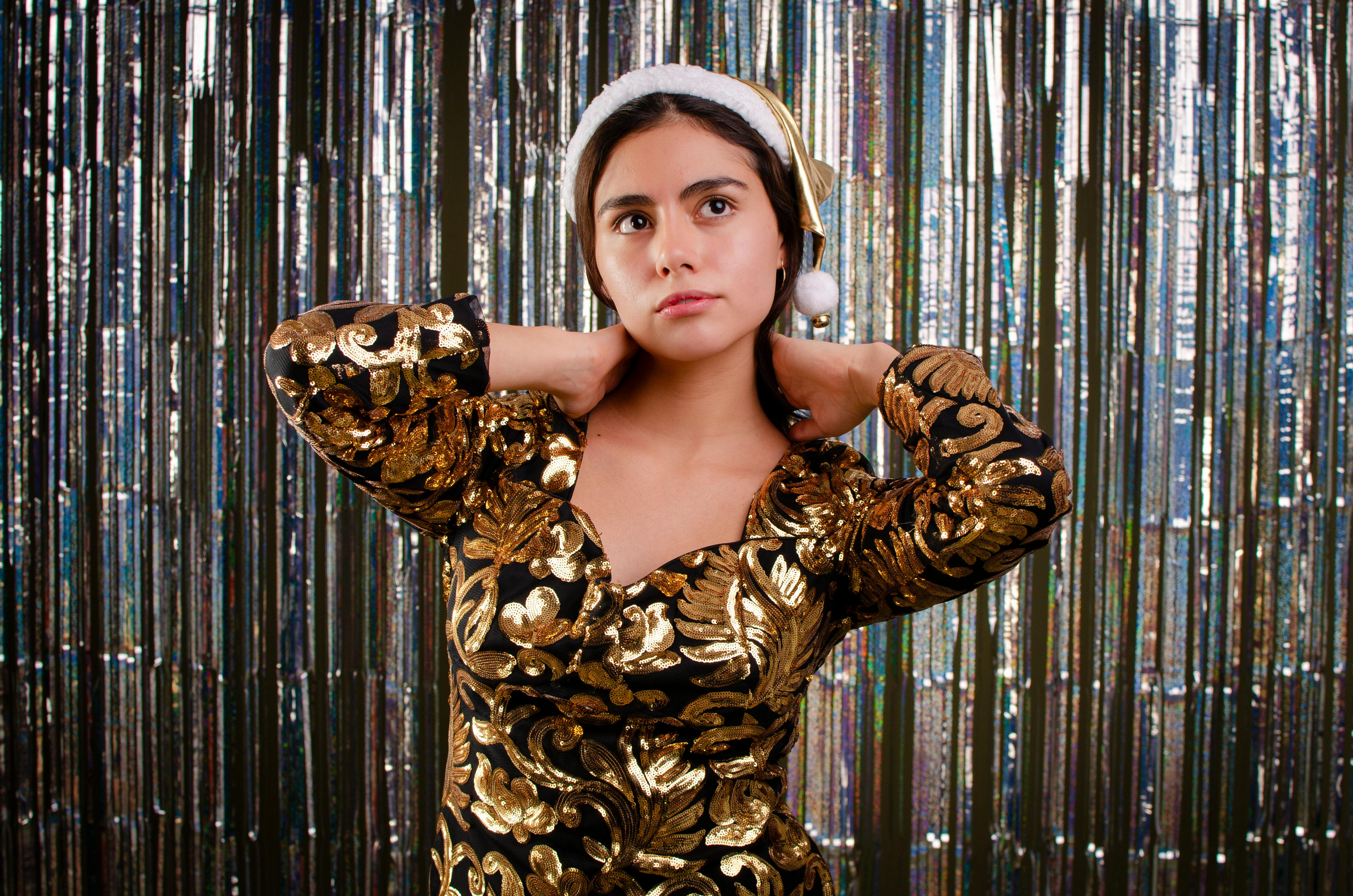 grátis Retrato sofisticado de uma mulher em um vestido dourado e chapéu de Papai Noel, pronta para a celebração. Foto profissional