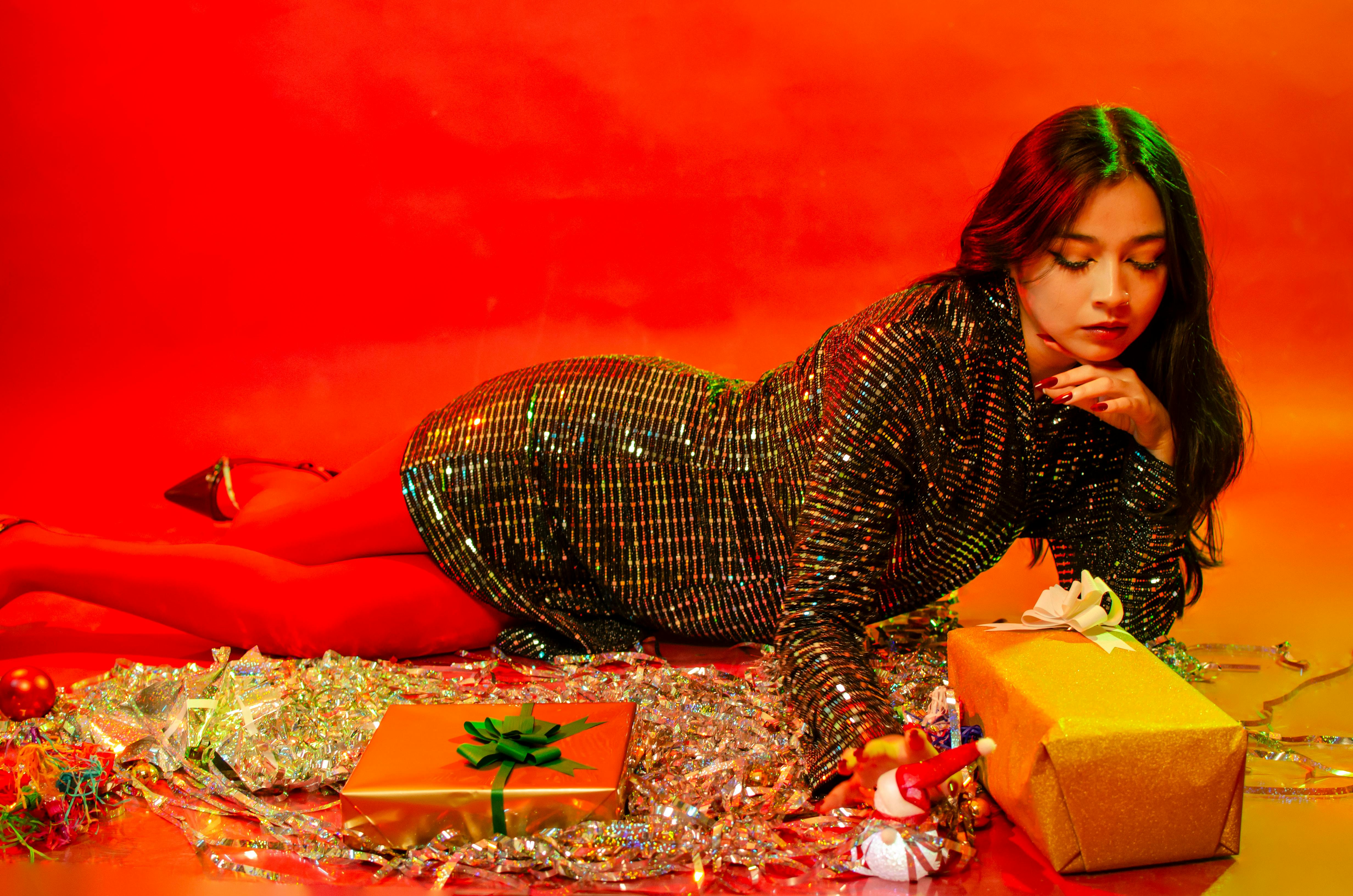 Kostenlos Model im schimmernden Outfit, umgeben von Weihnachtsgeschenken, strahlt festliche Eleganz aus. Stock-Foto