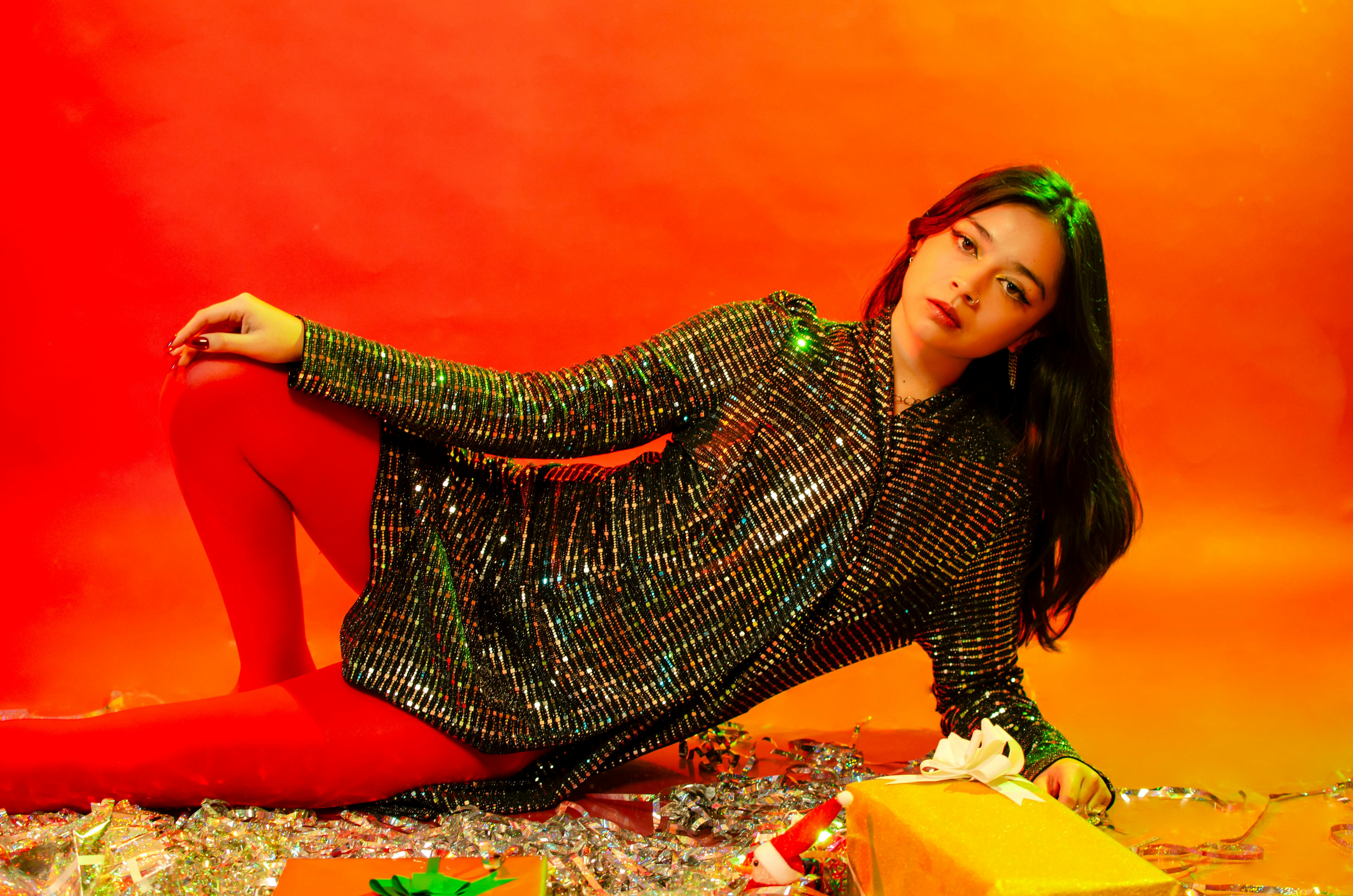 grátis Mulher estilosa em traje de lantejoulas deitada com presentes de Natal. Cenário vibrante e festivo. Foto profissional