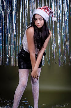 Young woman in festive attire with Santa hat and tinsel backdrop, celebrating holiday season.