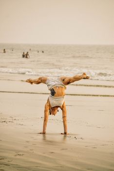 Man performs yoga handstand on a serene beach in Goa at sunset.
