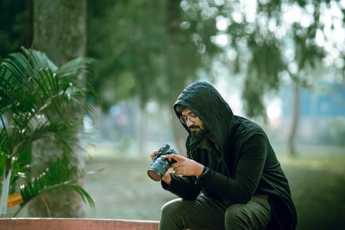 Free A photographer in a hooded jacket examines photos on his camera in a serene park. Stock Photo