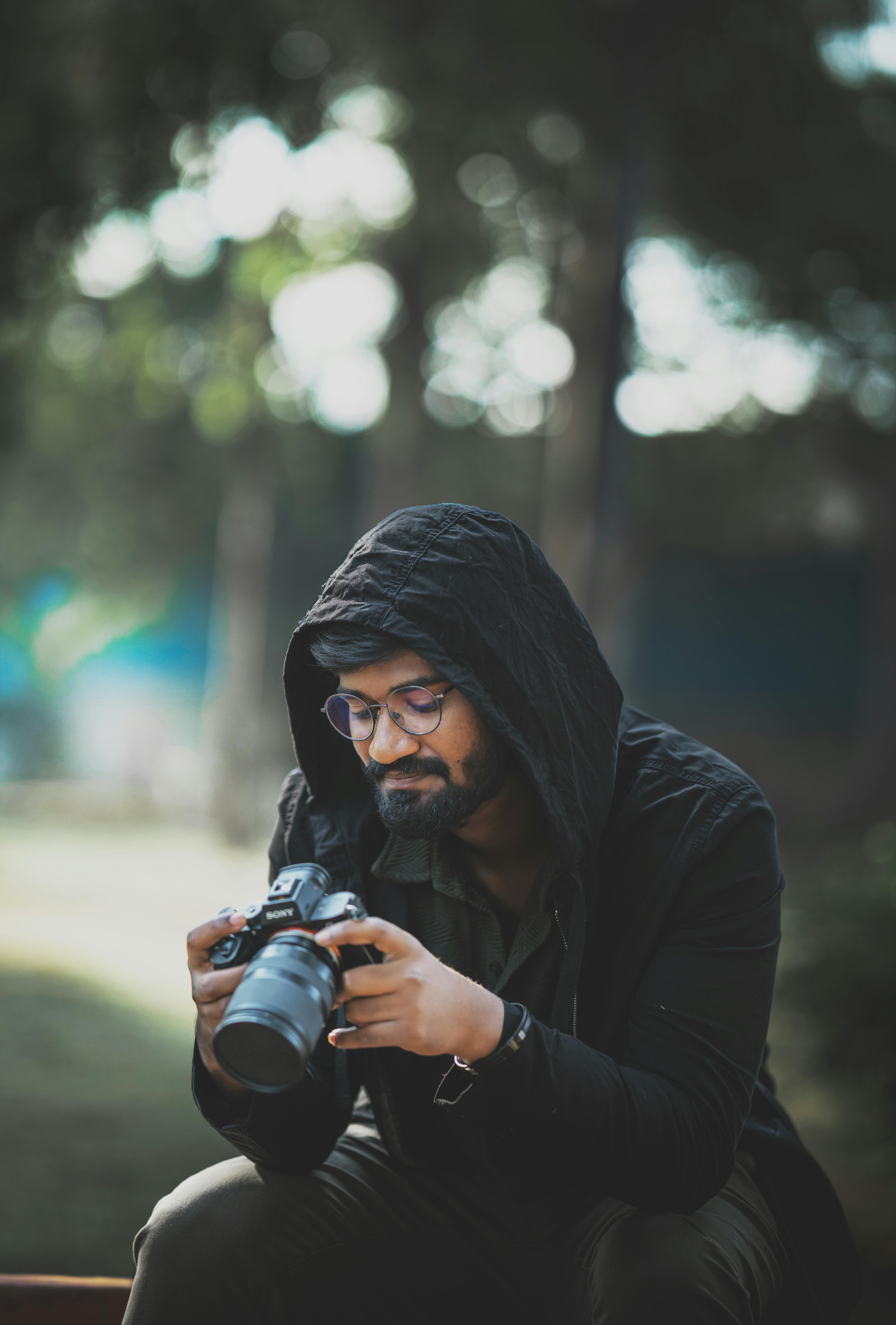 Gratuit Bărbat cu hanorac care inspectează o cameră DSLR într-un cadru în aer liber. Fotografie de stoc