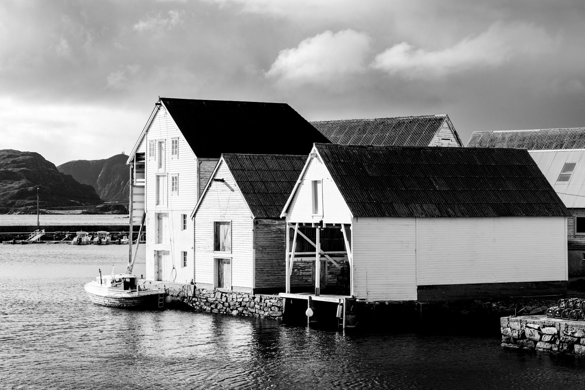 Black and white photo of a rustic waterfront warehouse in a serene landscape.