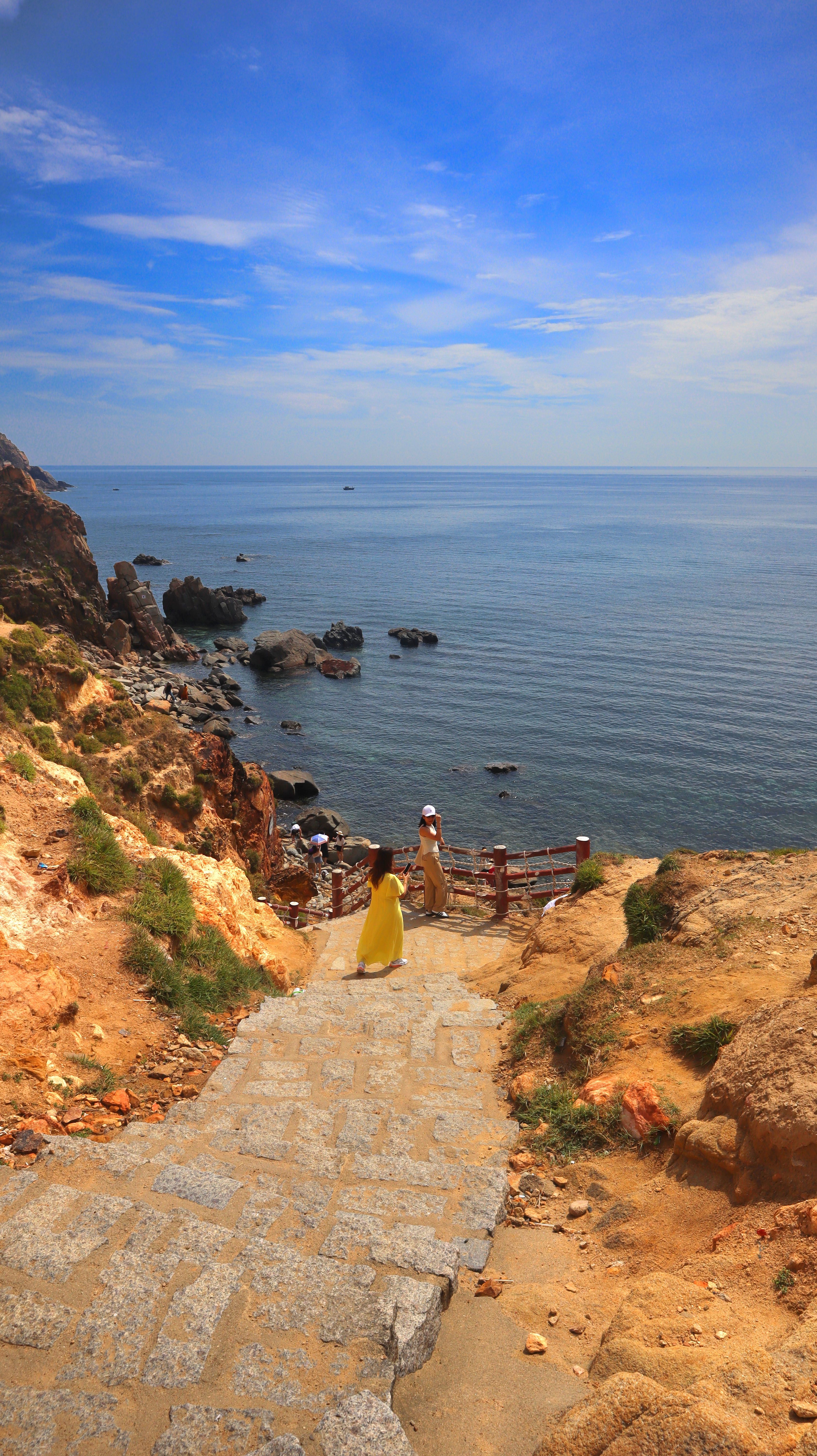Woman walks down a beach path overlooking the sea in Quy Nhon, Vietnam, on a sunny day.