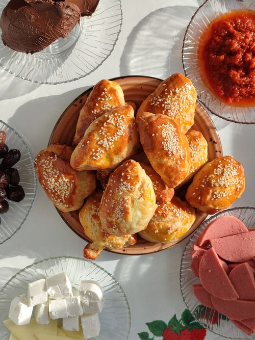 Free Fresh sesame bread rolls surrounded by feta, olives, sauce, and luncheon slices. Stock Photo