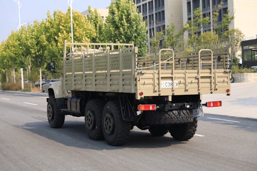 A rugged military cargo truck driving on an urban street lined with trees and buildings.
