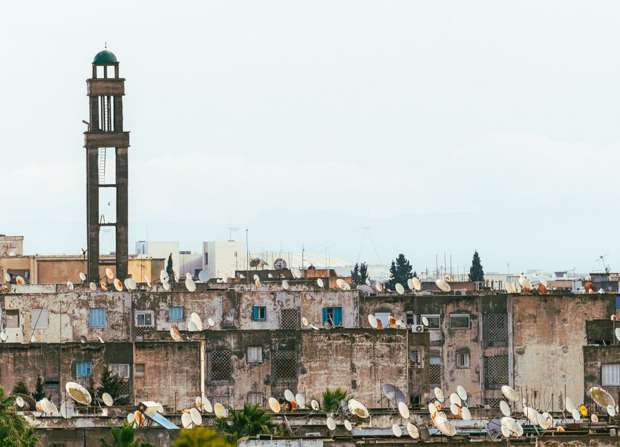 Urban rooftops with satellite dishes beneath a towering minaret in Tunis, Tunisia.
