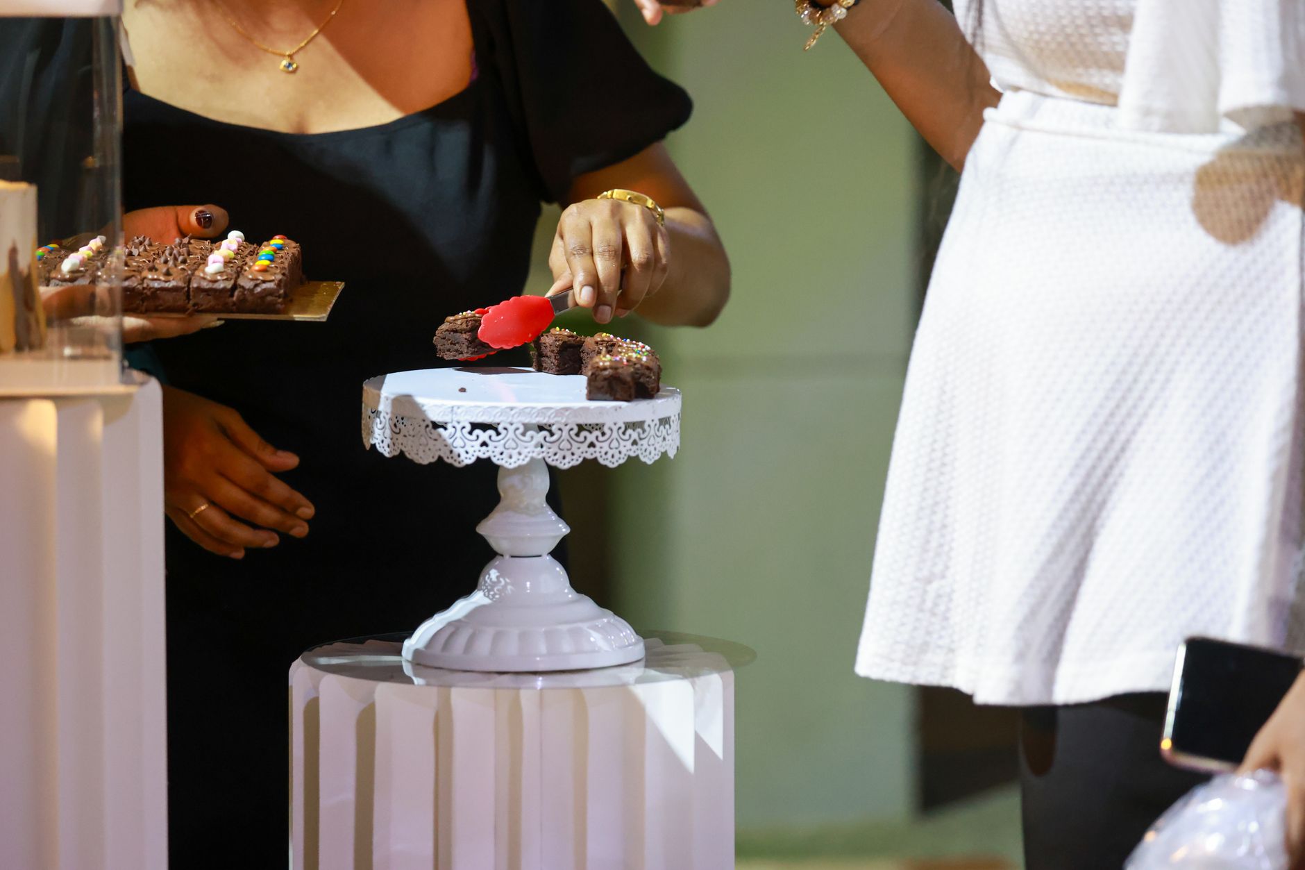 Guests serving chocolate brownies from an elegant dessert table at a social event.