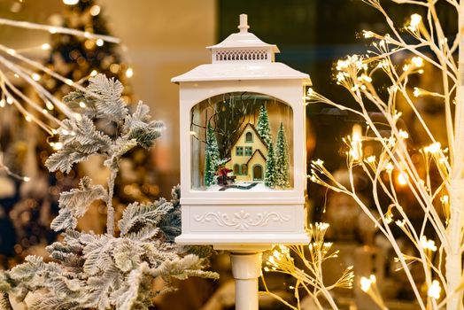 Charming winter lantern with miniature house surrounded by festive lights.