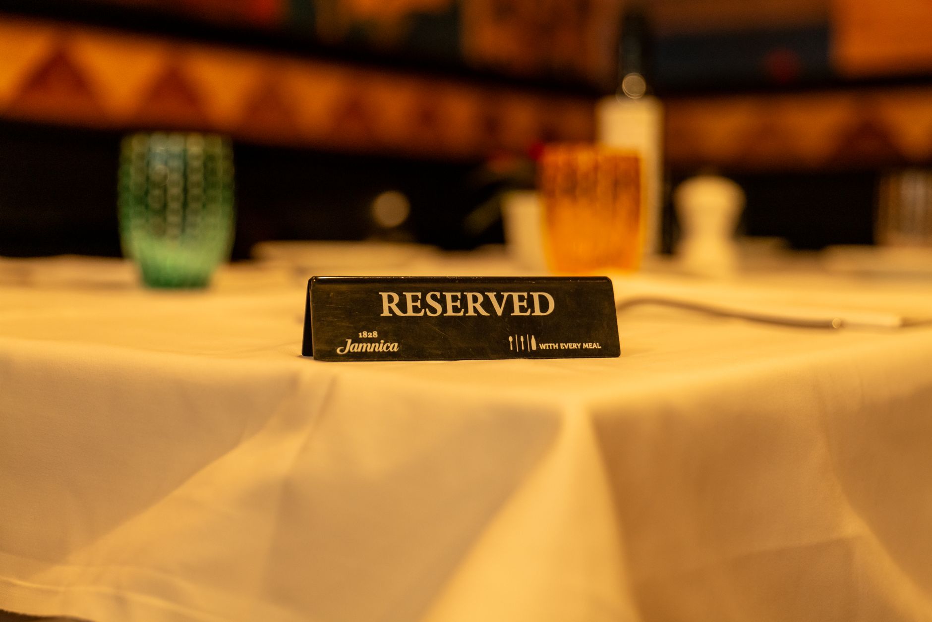 Close-up of a reserved sign on a white tablecloth in a dimly lit restaurant setting.
