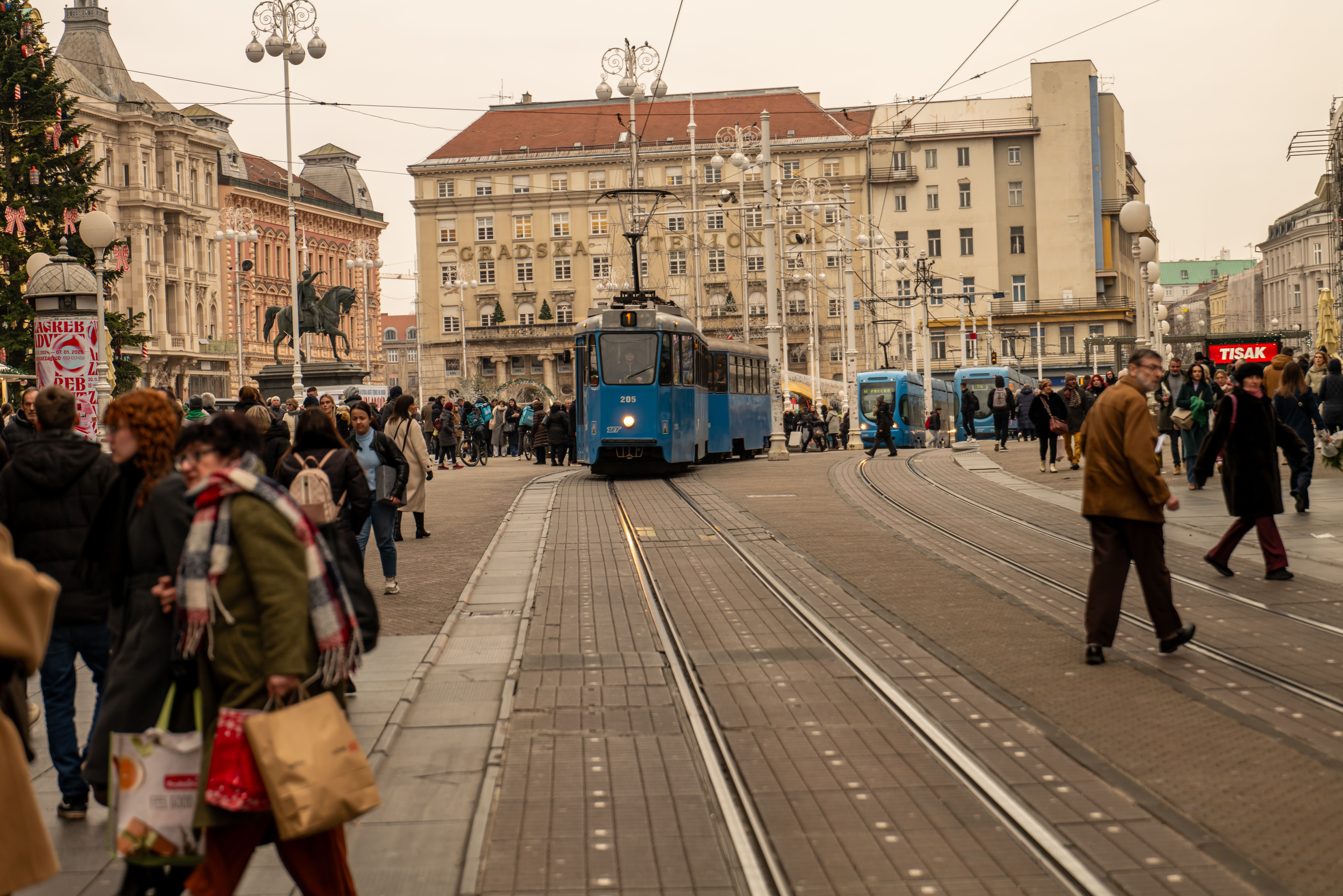 Bustling urban scene in Zagreb featuring a blue tram and pedestrians crossing the street.
