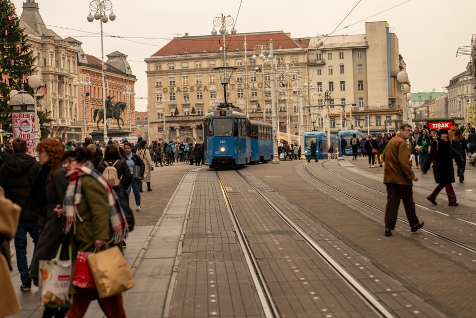 Bustling urban scene in Zagreb featuring a blue tram and pedestrians crossing the street.