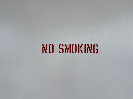 Simple 'No Smoking' sign stenciled on a blank grey wall, promoting a smoke-free environment.