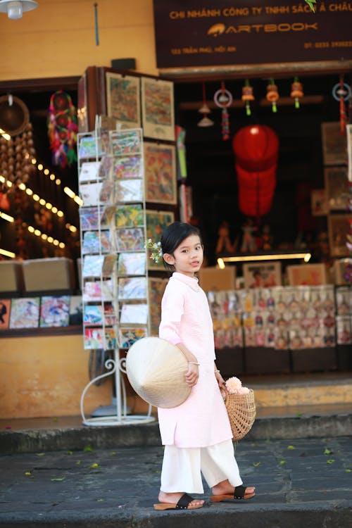 Free A child wearing a traditional áo dài in Hội An, Vietnam, holding a bamboo basket and conical hat. Stock Photo