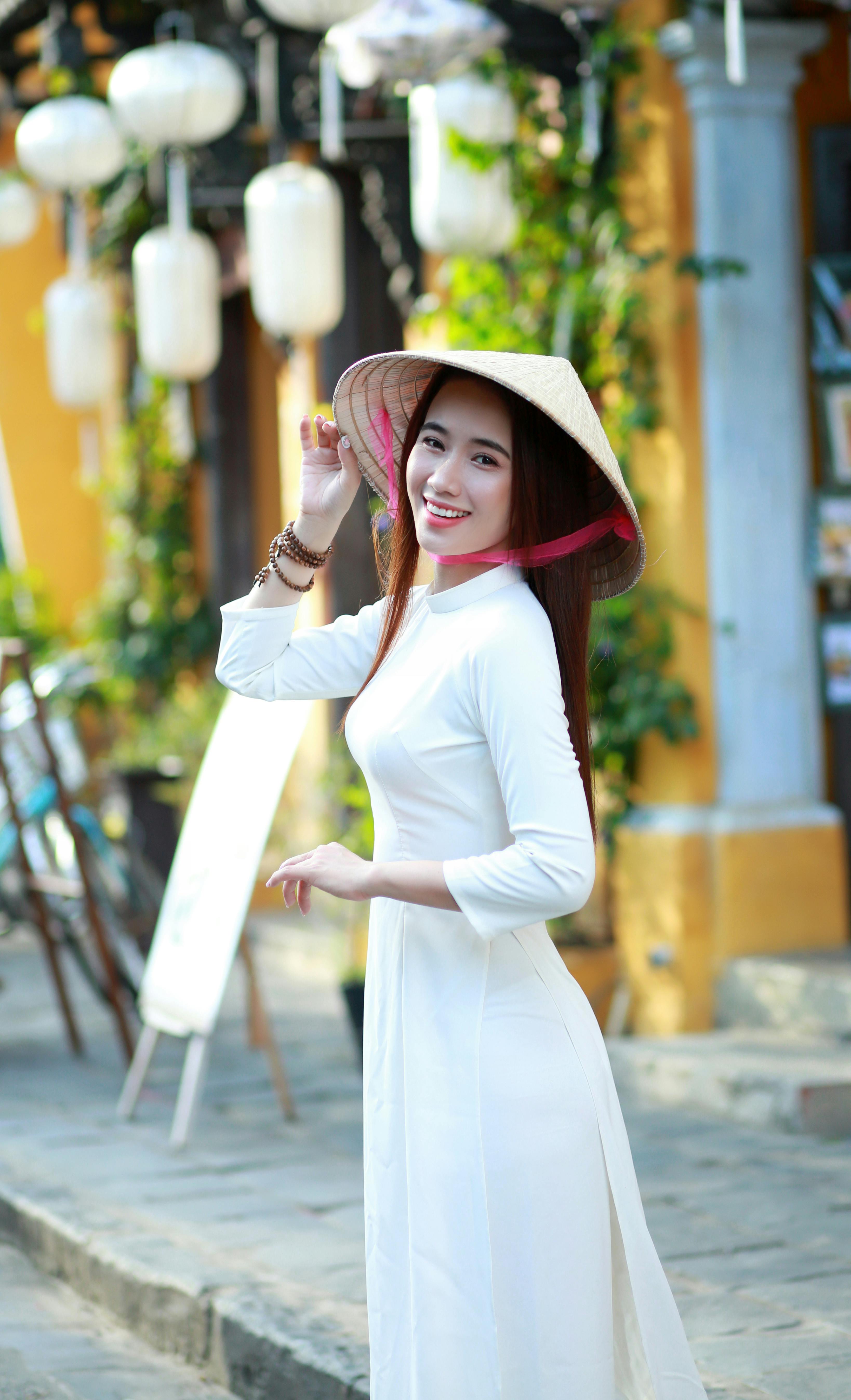 Elegant Vietnamese woman in ao dai and conical hat in Hội An street view.
