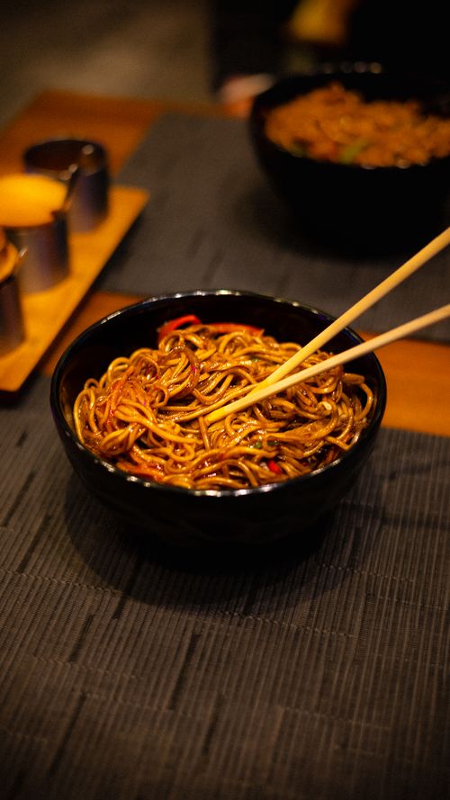 Free A close-up of tasty noodles in a black bowl with chopsticks on a table ready to eat. Stock Photo