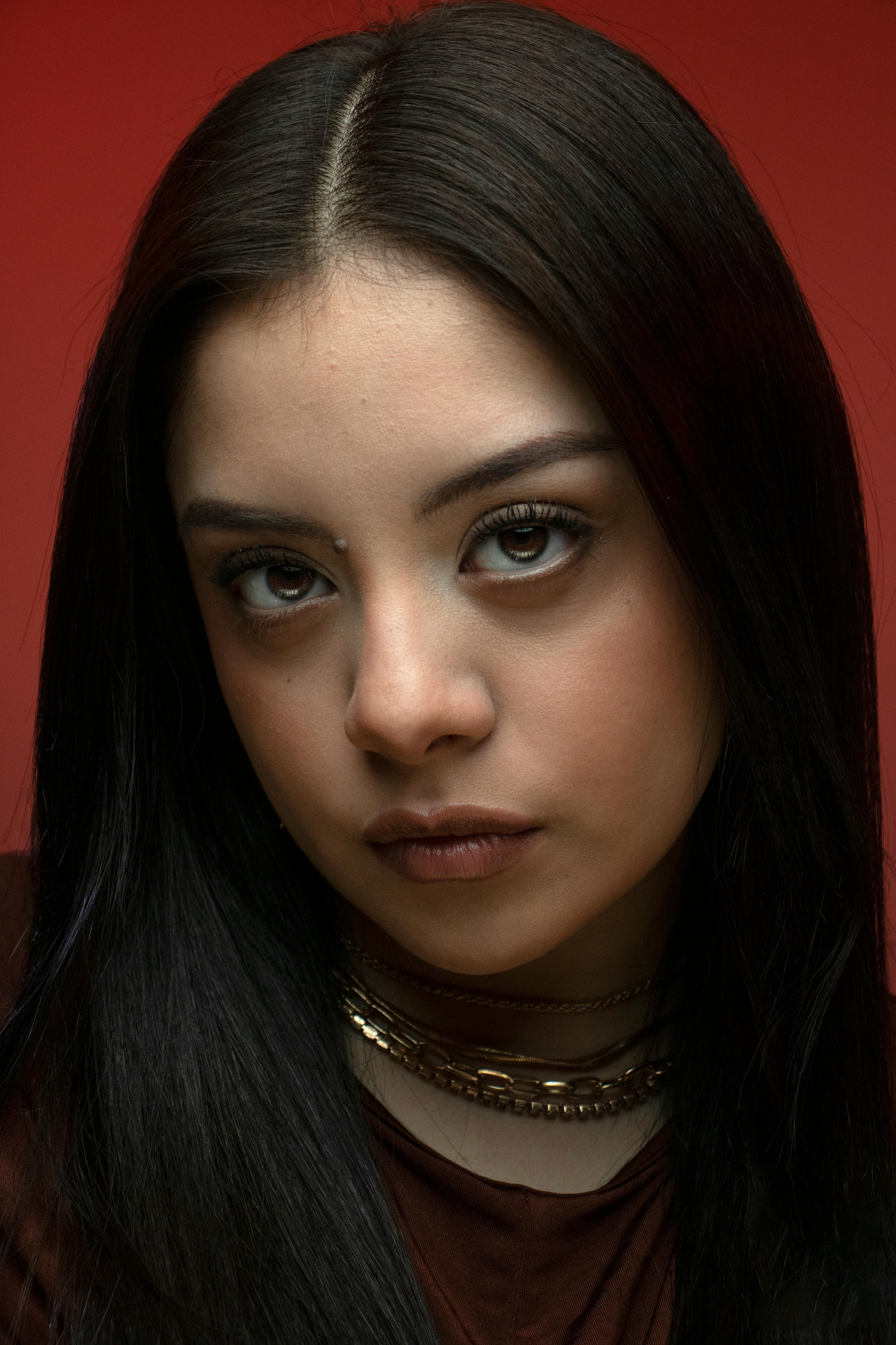 Close-up portrait of a young woman with long dark hair on a red background.
