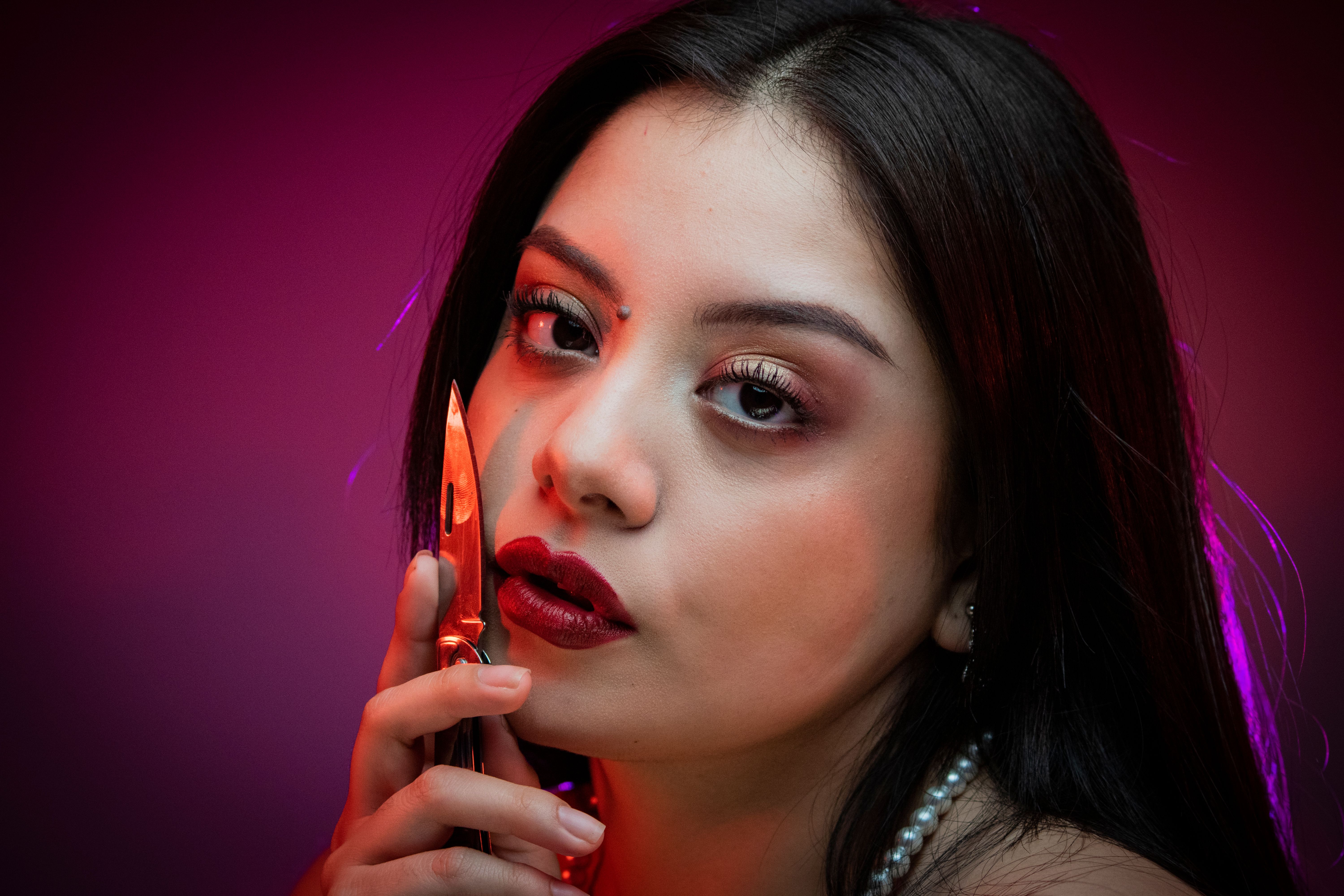 Intense portrait of a woman holding a knife against a colorful backdrop.