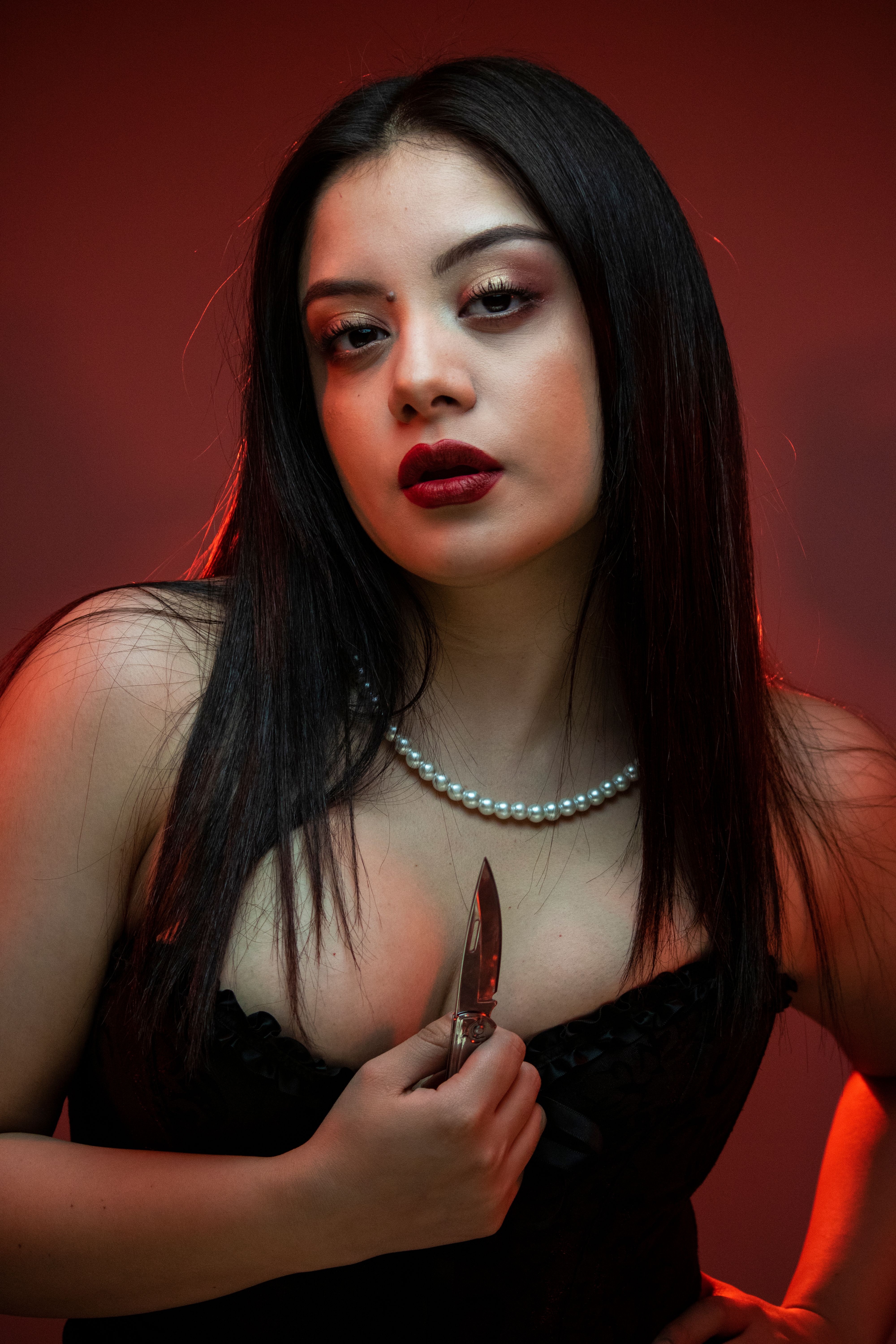 Moody portrait of a woman holding a knife with red lighting and dramatic expression.