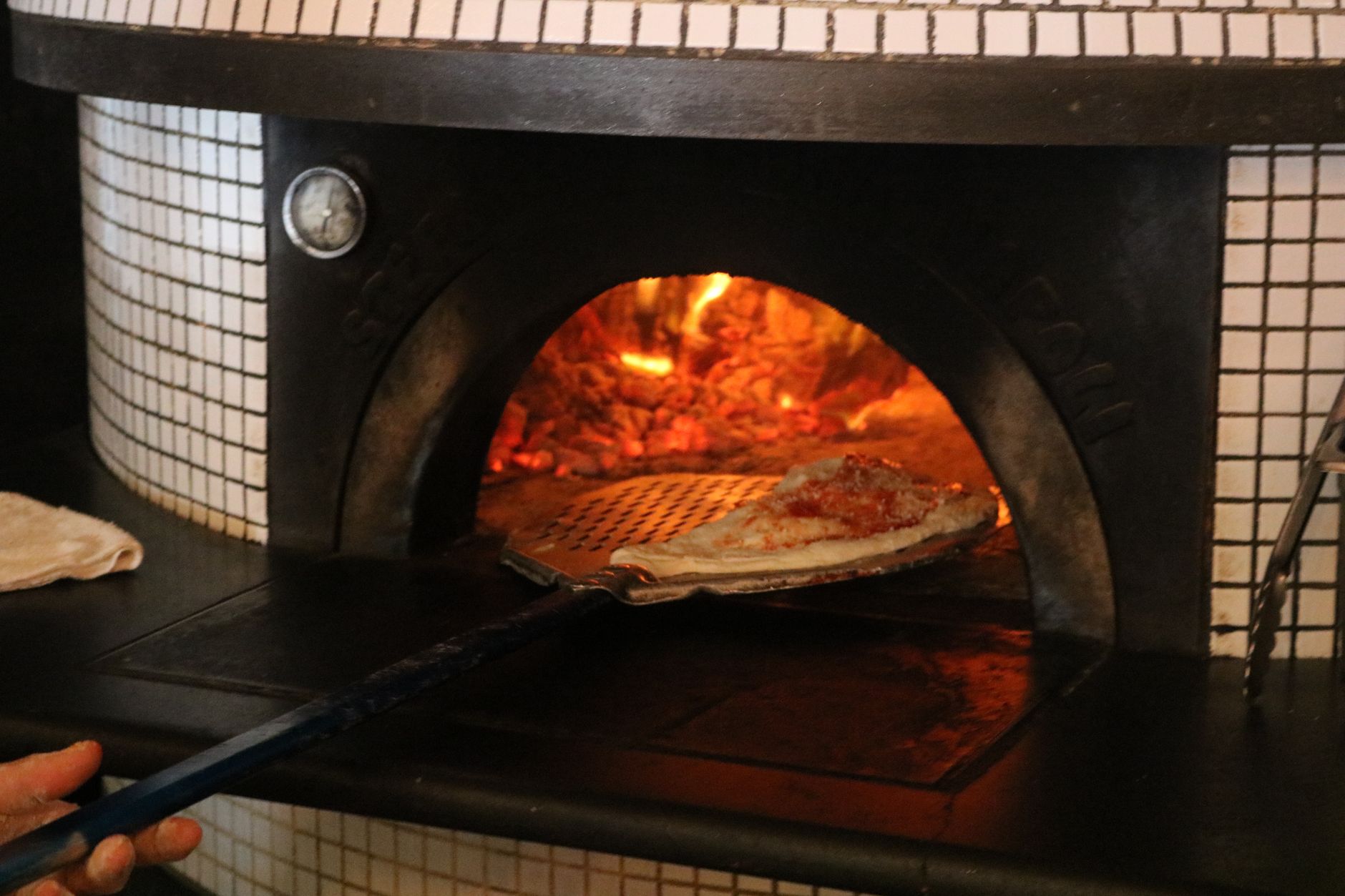 Close-up of a pizza being baked in a traditional wood-fired oven, showcasing culinary authenticity.