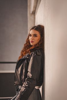Portrait of a young woman in a leather jacket against a wall.