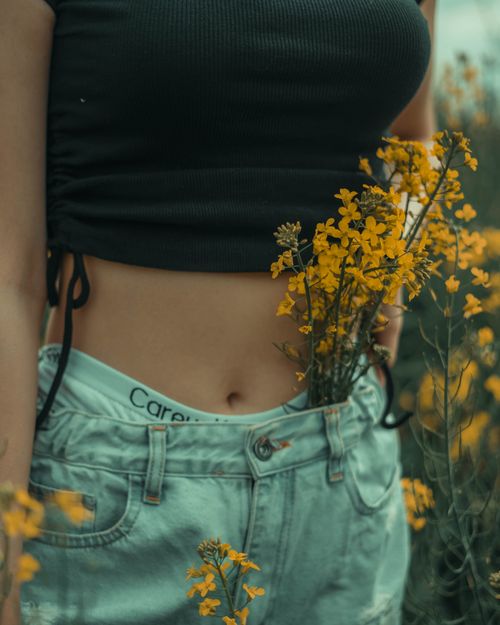 Free A young woman with yellow flowers tucked in her jeans standing outdoors in a field. Stock Photo