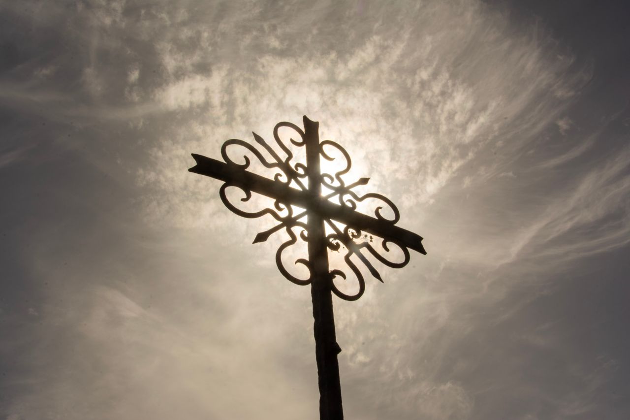 a decorative wrought iron cross presents an artistic silhouette agains