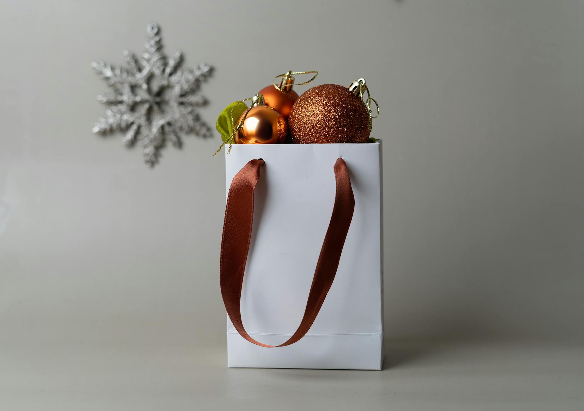 Elegant gift bag filled with Christmas ornaments and a snowflake in the background.