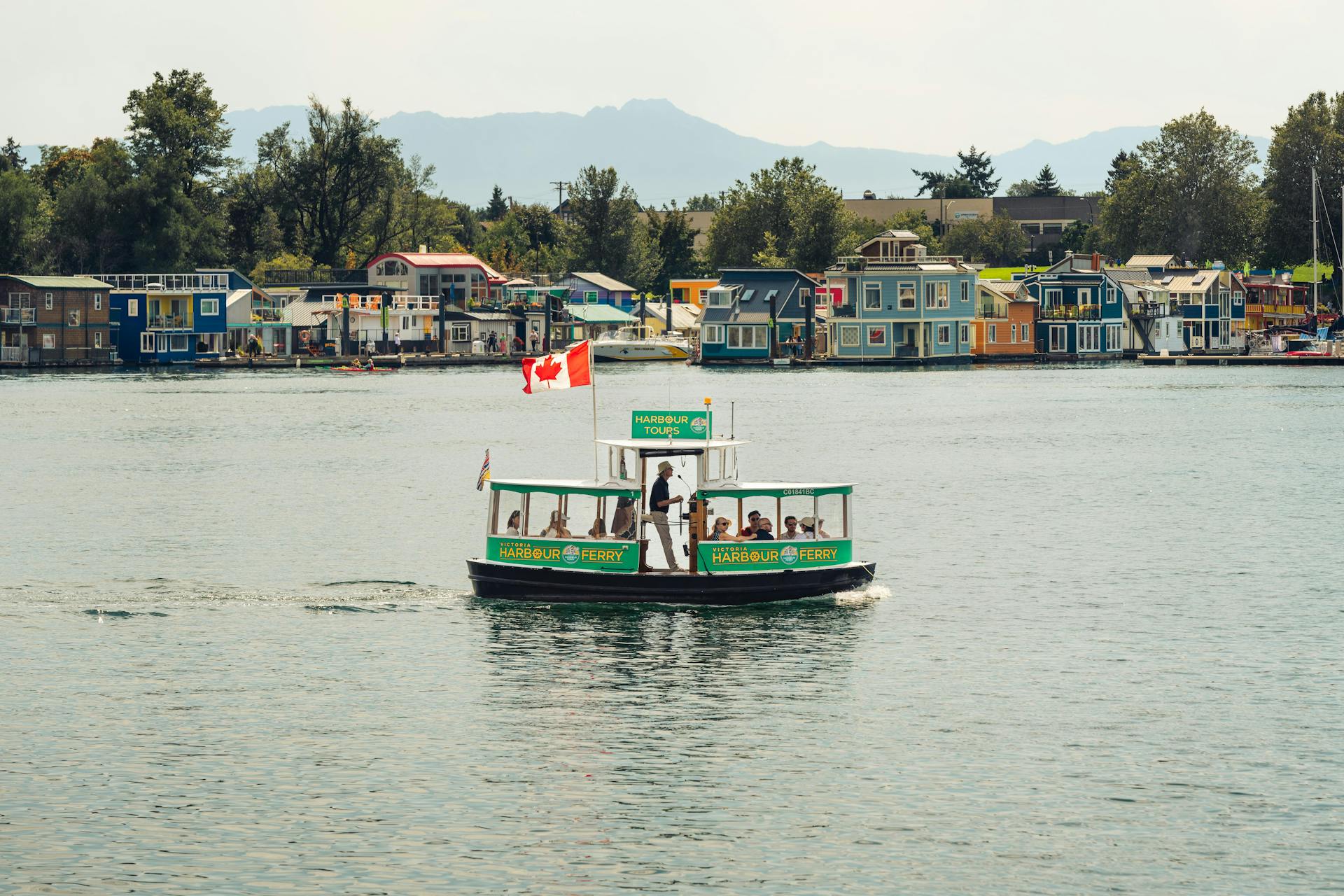 Scenic ferry tour in Victoria's Inner Harbour, British Columbia with vibrant houseboats and distant mountains.