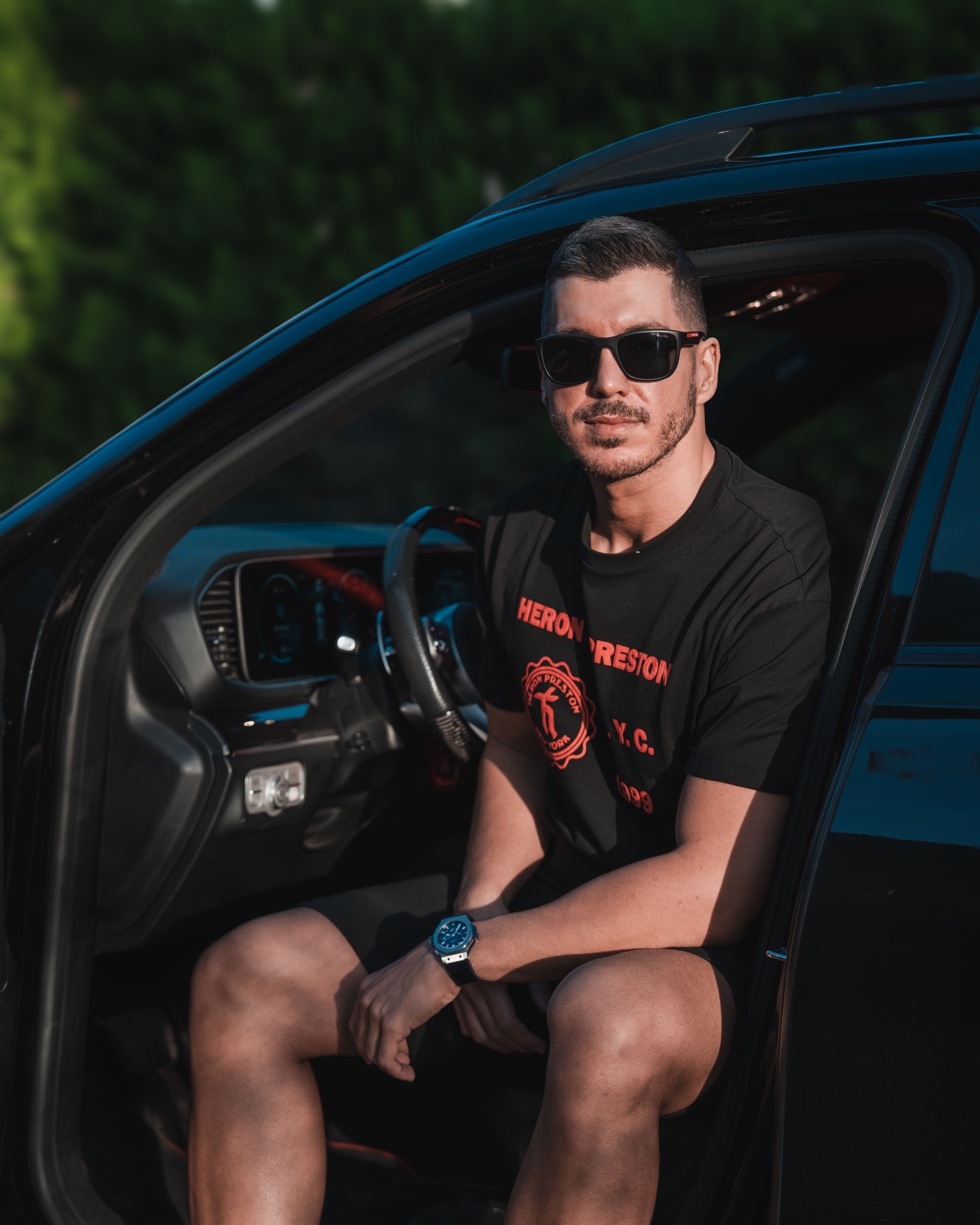 Young man sitting in car, wearing sunglasses on a sunny day.