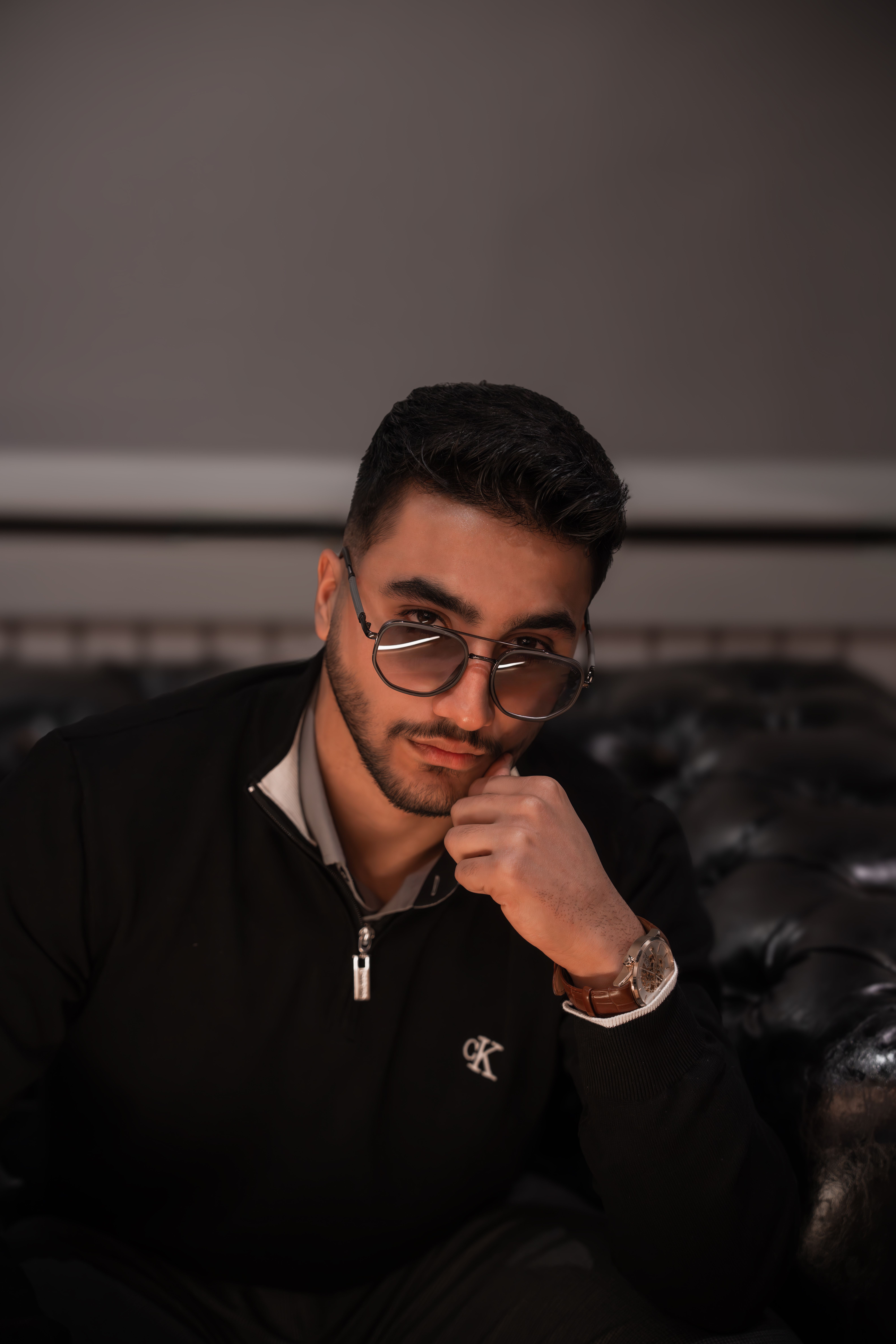 Portrait of a stylish young man wearing sunglasses indoors, seated thoughtfully.