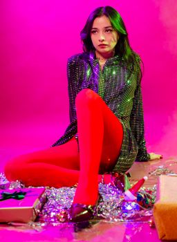 Stylish woman in sparkly outfit poses with Christmas gifts and decorations.